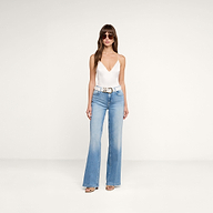 A woman wearing sunglasses, the Dara Stretch Satin Bodysuit—a white sleeveless V-neck top with adjustable straps and a satin base layer—paired with light blue high-waisted flared jeans, a white belt, and sandals, stands against a plain white background.