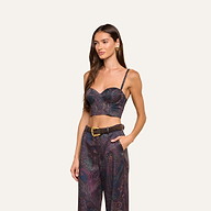 A woman stands against a plain light background, one hand in her pocket, wearing the Sonya Bustier in navy paisley with built-in support, paired with matching high-waisted pants and a brown belt.