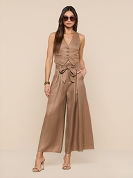 Woman wearing sunglasses, the Jianna Vest—a sleeveless linen style—wide-leg high-waisted pants with a bow belt, and heeled sandals stands against a plain white background.