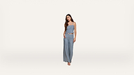 A woman stands against a plain white background, wearing a blue strapless top and matching wide-leg pants. She has long dark hair and neutral sandals, with one hand resting on her hip.
