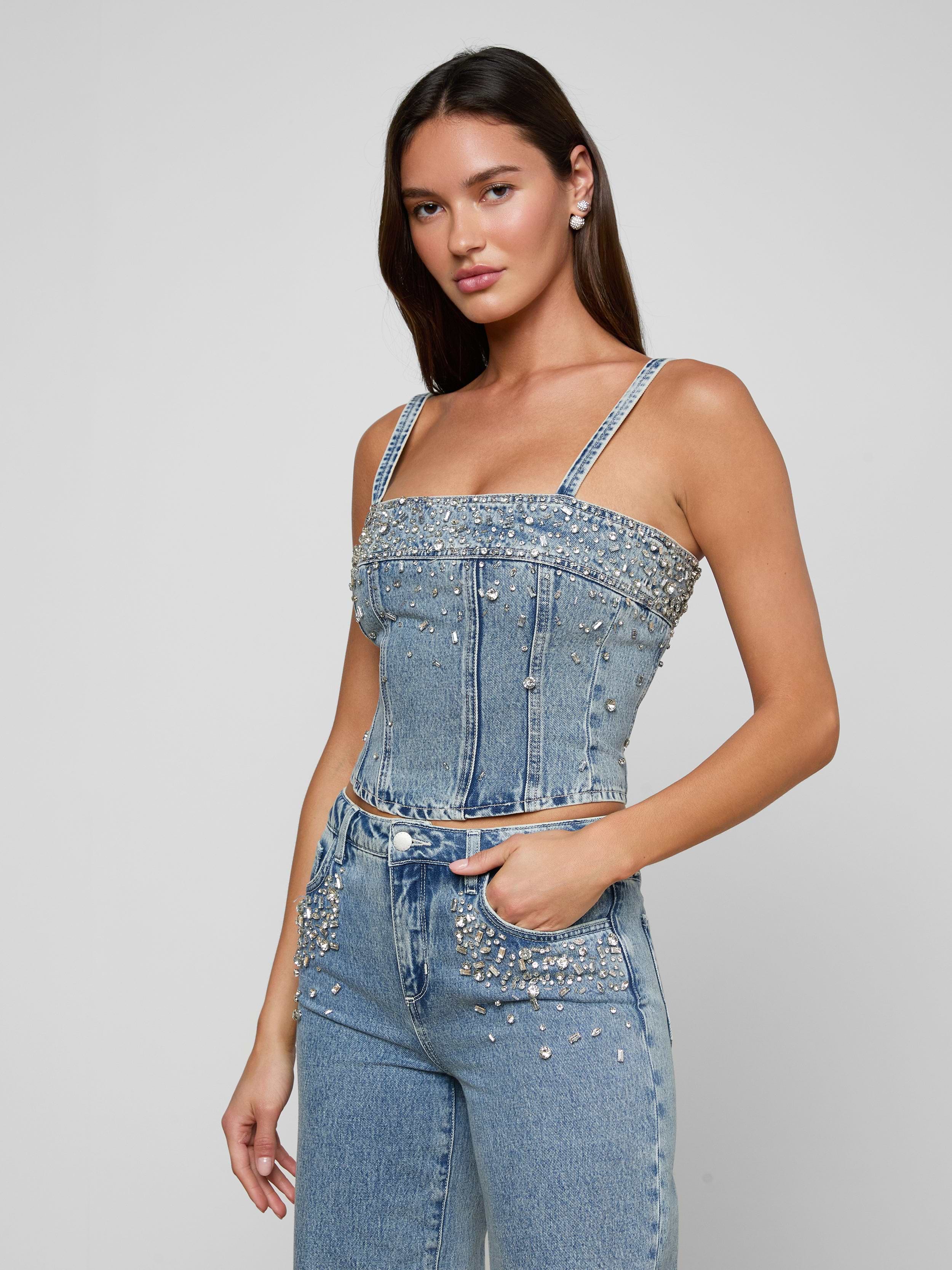 Wearing the Arlin Embellished Tank and cropped jeans adorned with pearls and rhinestones, a woman stands with one hand in her pocket against a plain background.