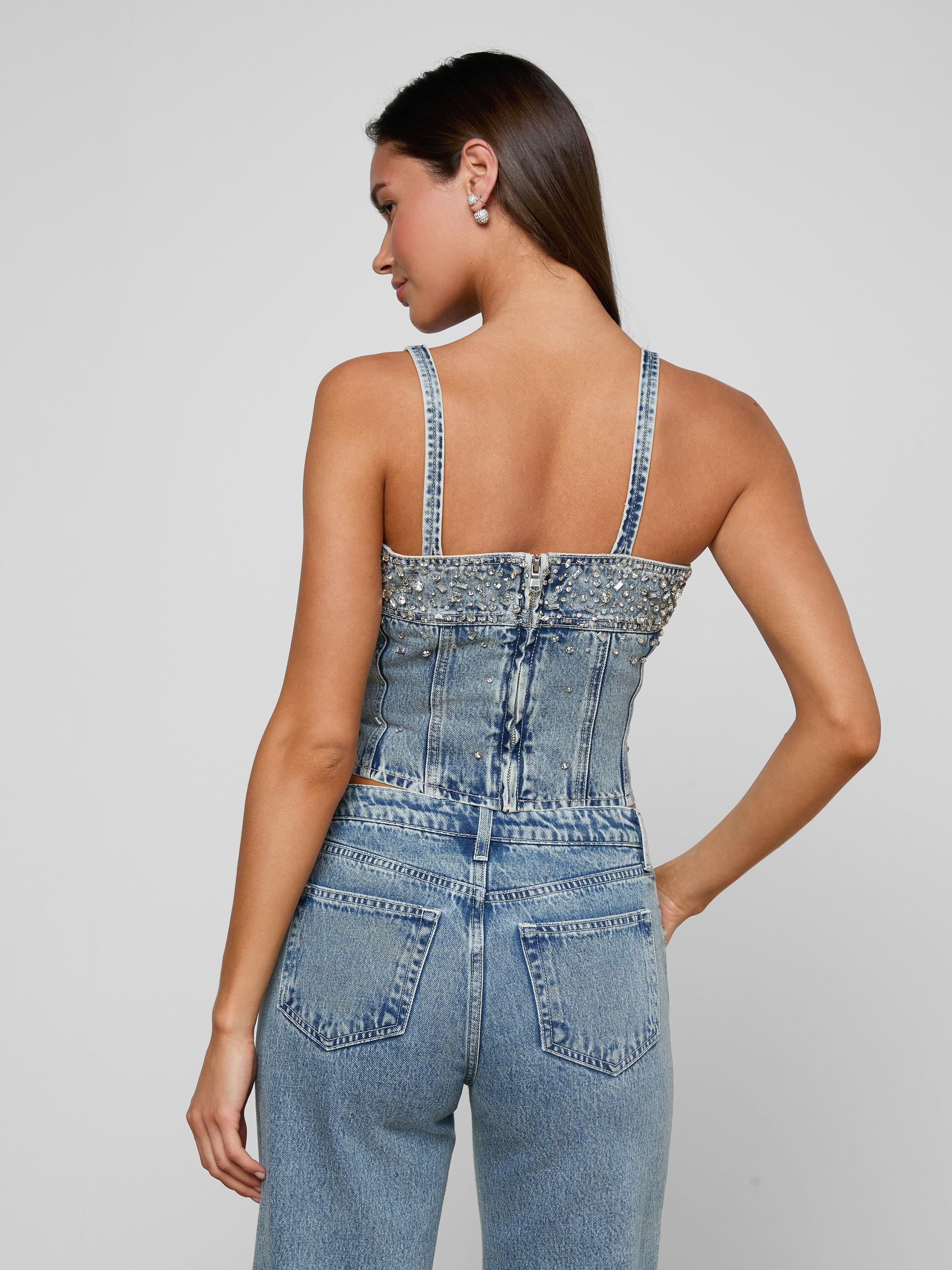 Woman with long dark hair, wearing the Arlin Embellished Tank and high-waisted blue jeans, standing with her back to the camera against a plain light background.