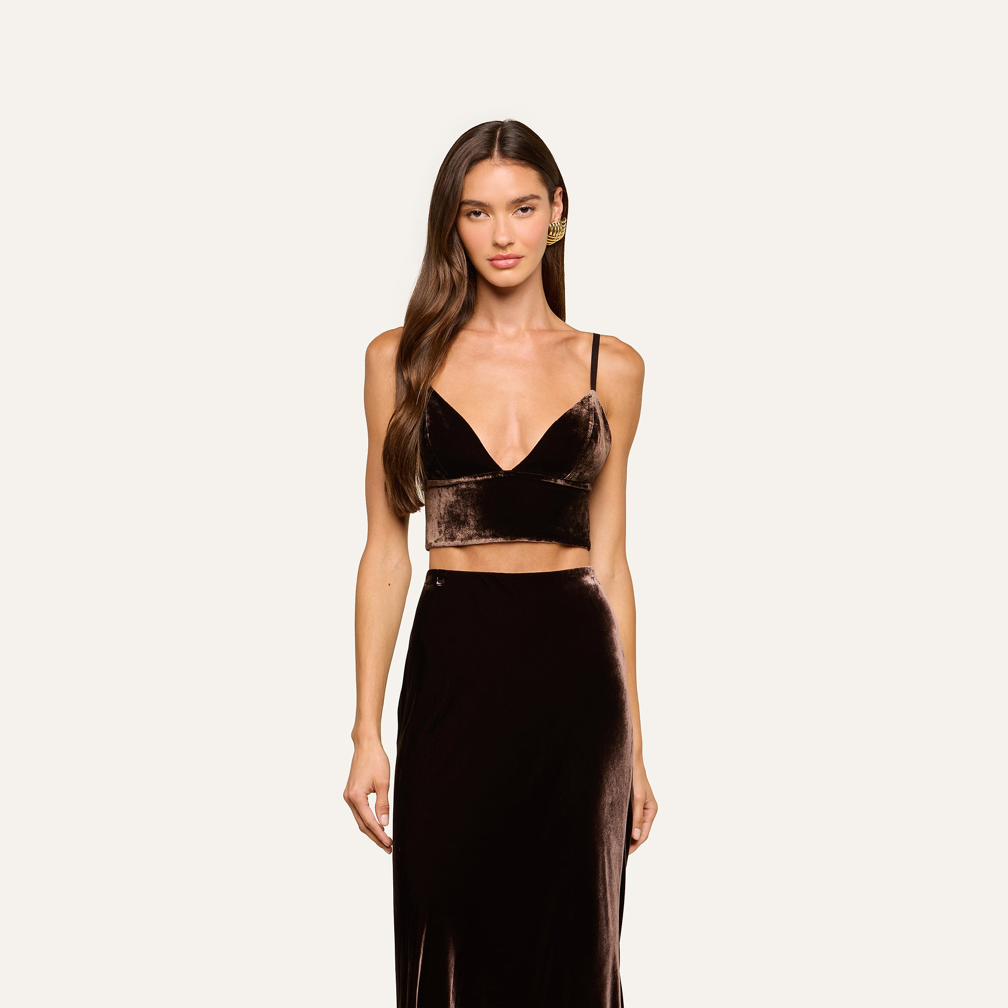 A woman with long brown hair wears the Aislin Velvet Bralette in java brown with adjustable straps, paired with a matching high-waisted skirt, standing against a plain light background and looking at the camera with a neutral expression.
