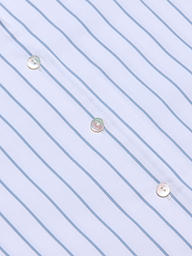 Close-up of the Deon Tie-Neck Blouse, crafted from an organic cotton-blend white fabric with thin blue vertical stripes and featuring three shiny white buttons sewn diagonally across the material.