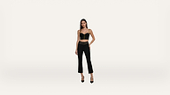 A woman wearing a black crop top, black high-waisted pants, and black heels stands against a plain white background, with one hand on her hip.