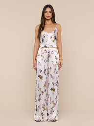 A woman with long brown hair wears the Charmy Satin Camisole, a sleeveless white top featuring a colorful butterfly print, standing against a plain white background.