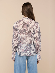 A woman with long brown hair is shown from the back against a plain light background, wearing the Eunice Blouse featuring a butterfly print and paired with light blue jeans.