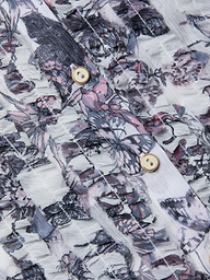 Close-up of the Eunice Blouse fabric featuring a pink, purple, and gray floral pattern, with two beige buttons bordered by gold rims sewn onto it. The textured, slightly sheer material showcases visible stitching lines—details reminiscent of those found on ruffled cuffs or butterfly print blouses.