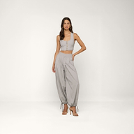 A woman stands in a studio wearing the Arwen Vest—a light gray cropped vest with buttons—paired with matching baggy pants cinched at the ankles and high-heeled sandals. The background is plain and white.