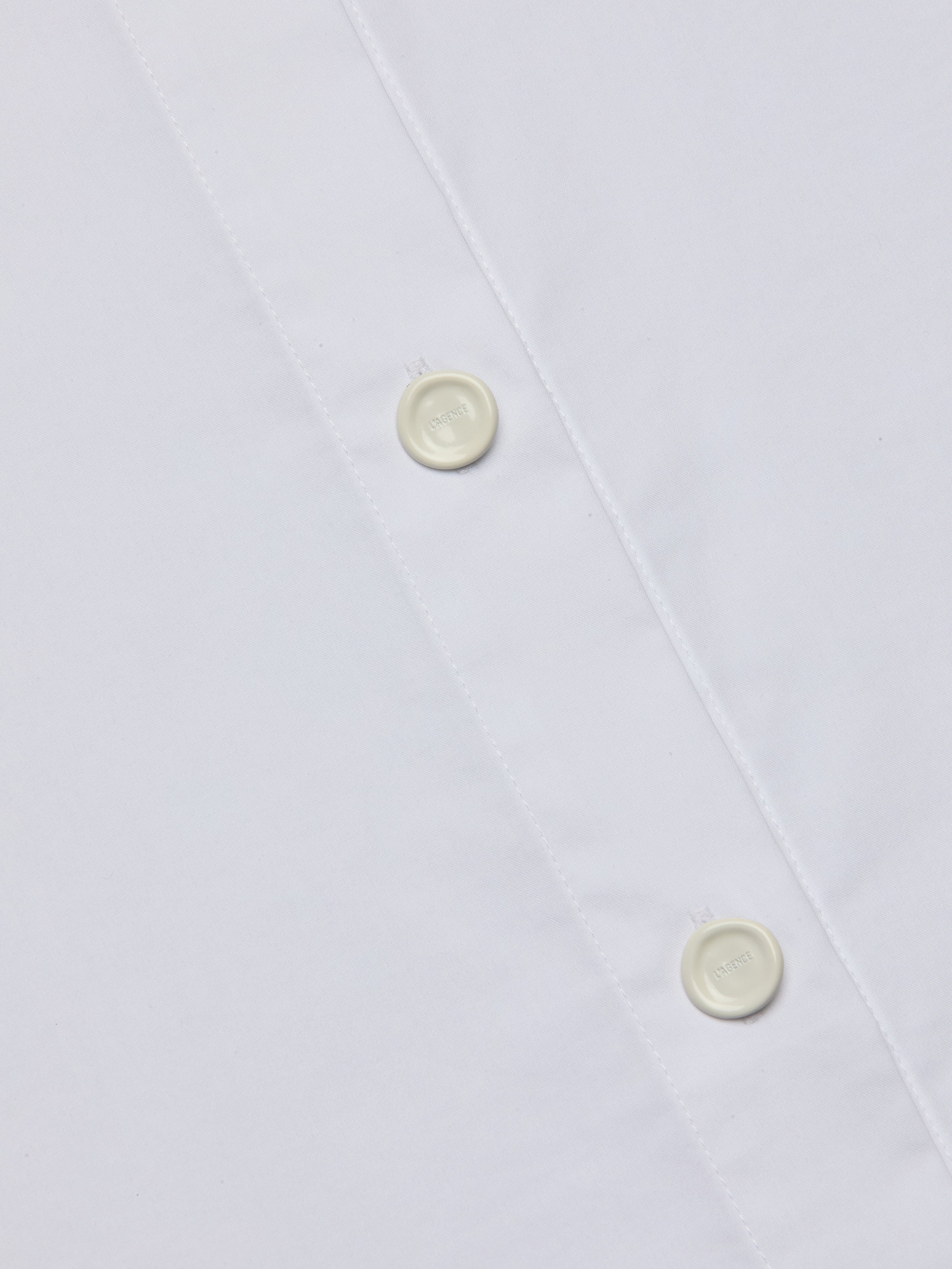Close-up of the Rylie Poplin Shirt, a white button-down dress shirt crafted from smooth, clean fabric, featuring two white buttons and visible stitching along the placket for a refined finish.