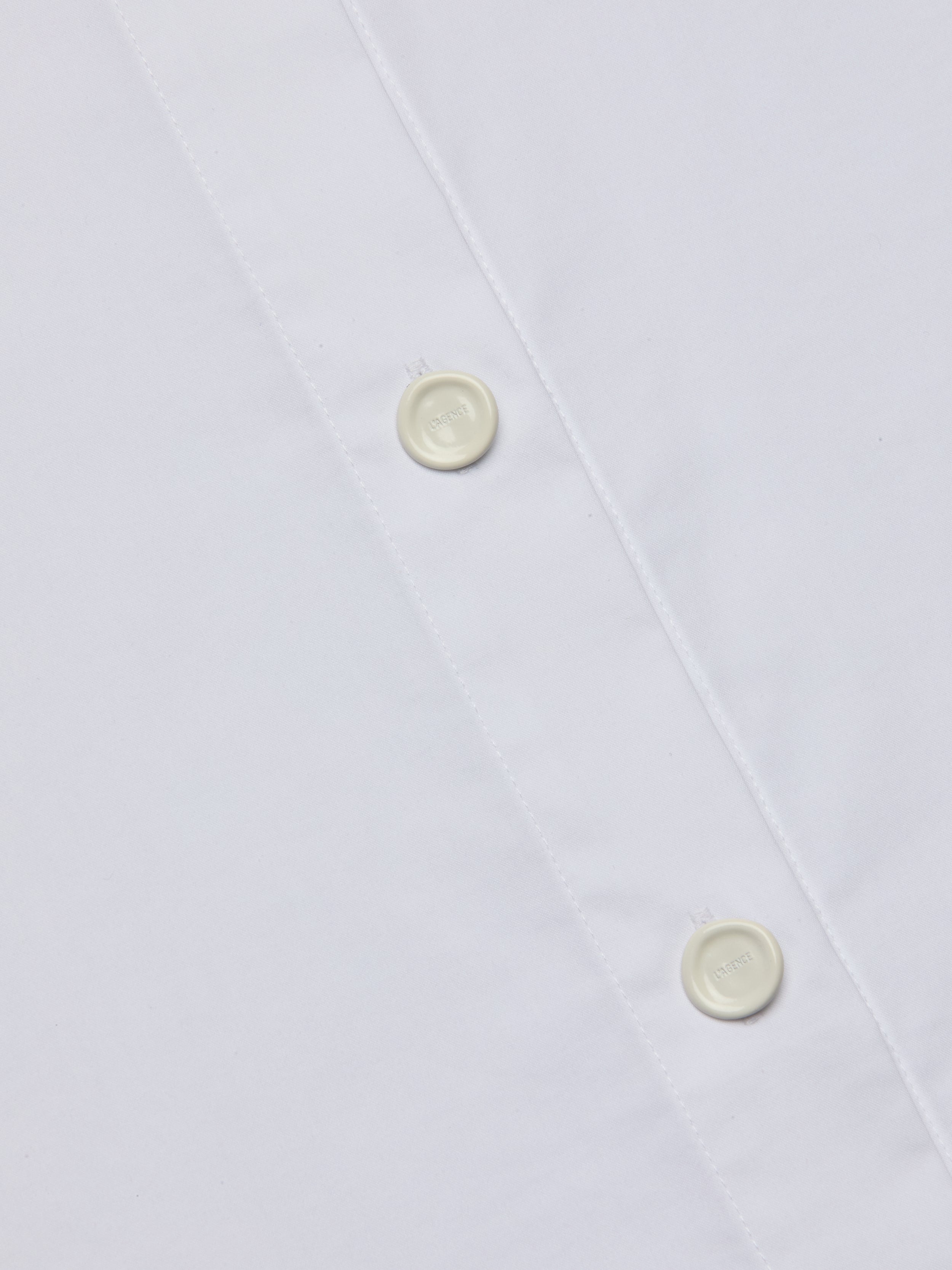 Close-up of the Rylie Poplin Shirt, a white button-down dress shirt crafted from smooth, clean fabric, featuring two white buttons and visible stitching along the placket for a refined finish.