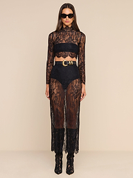 Woman stands against a plain white background wearing the sheer black Henriette Cropped Lace Top with scalloped hems, high-waisted black shorts, a black bandeau, black boots, a wide belt with a gold buckle, and dark sunglasses.