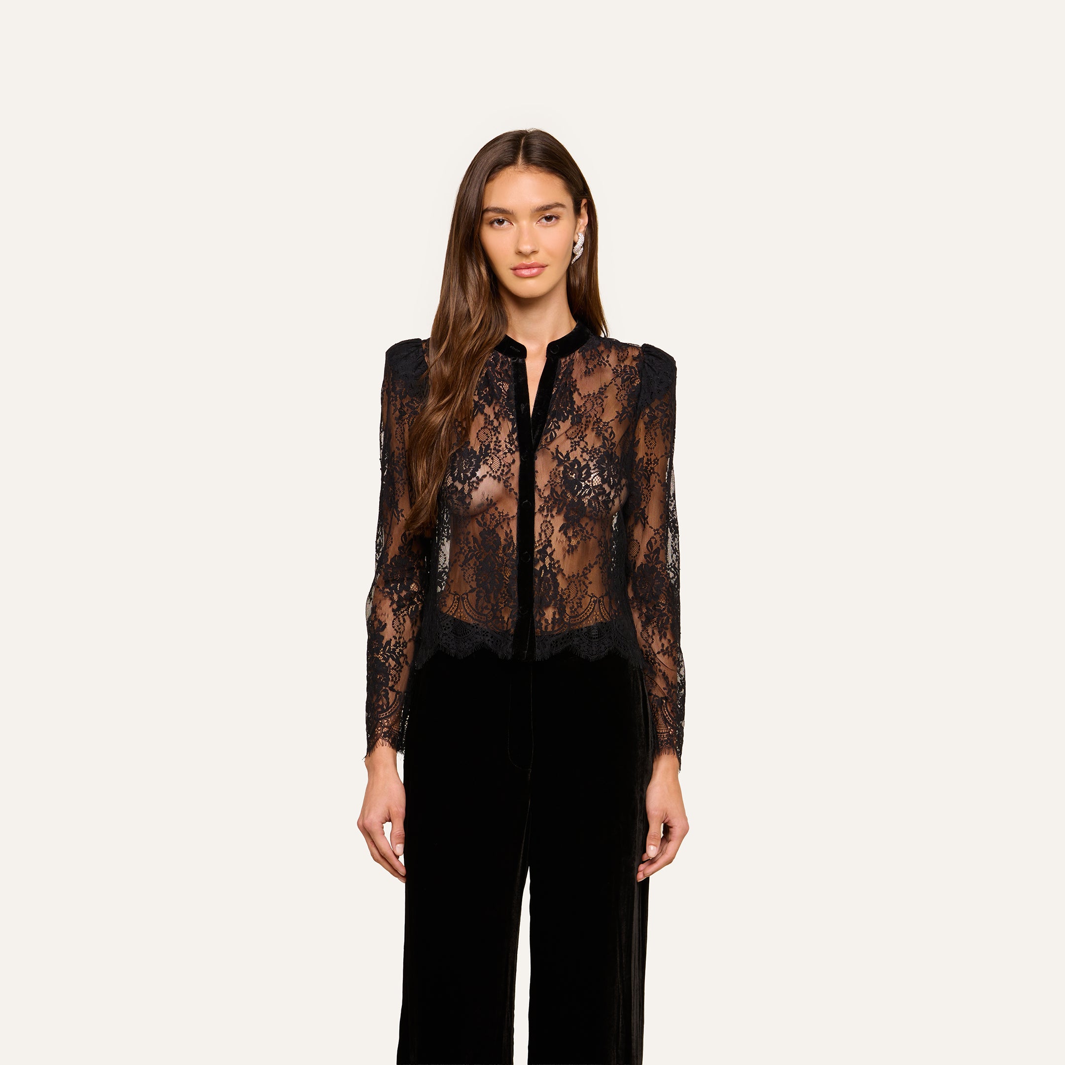 A woman stands facing forward, wearing the Dorothea Velvet Lace Blouse with long sleeves and Chantilly lace details, paired with black pants. She is set against a plain light background.