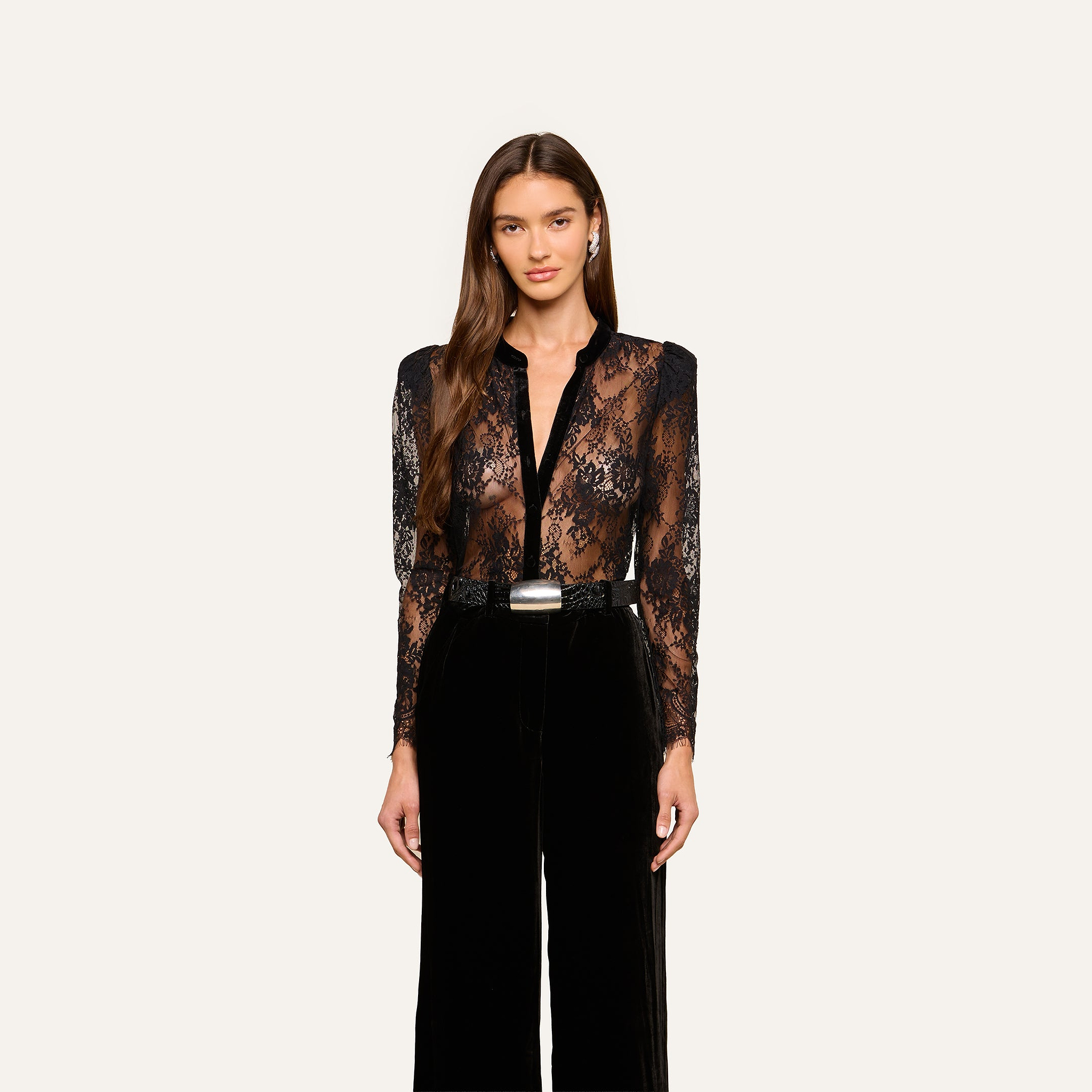 A woman wearing the Dorothea Velvet Lace Blouse with long sleeves, paired with high-waisted black pants, stands against a plain light background.