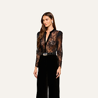 A woman with long brown hair wears the Dorothea Velvet Lace Blouse, paired with black high-waisted pants, a black belt with a silver buckle, and drop earrings, standing against a plain light background.