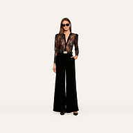 Wearing the Dorothea Velvet Lace Blouse, a woman in sunglasses stands confidently with one hand in her pocket, showcasing its sheer Chantilly lace long sleeves tucked into high-waisted, wide-leg black velvet pants with elegant velvet seams and finished with black shoes.