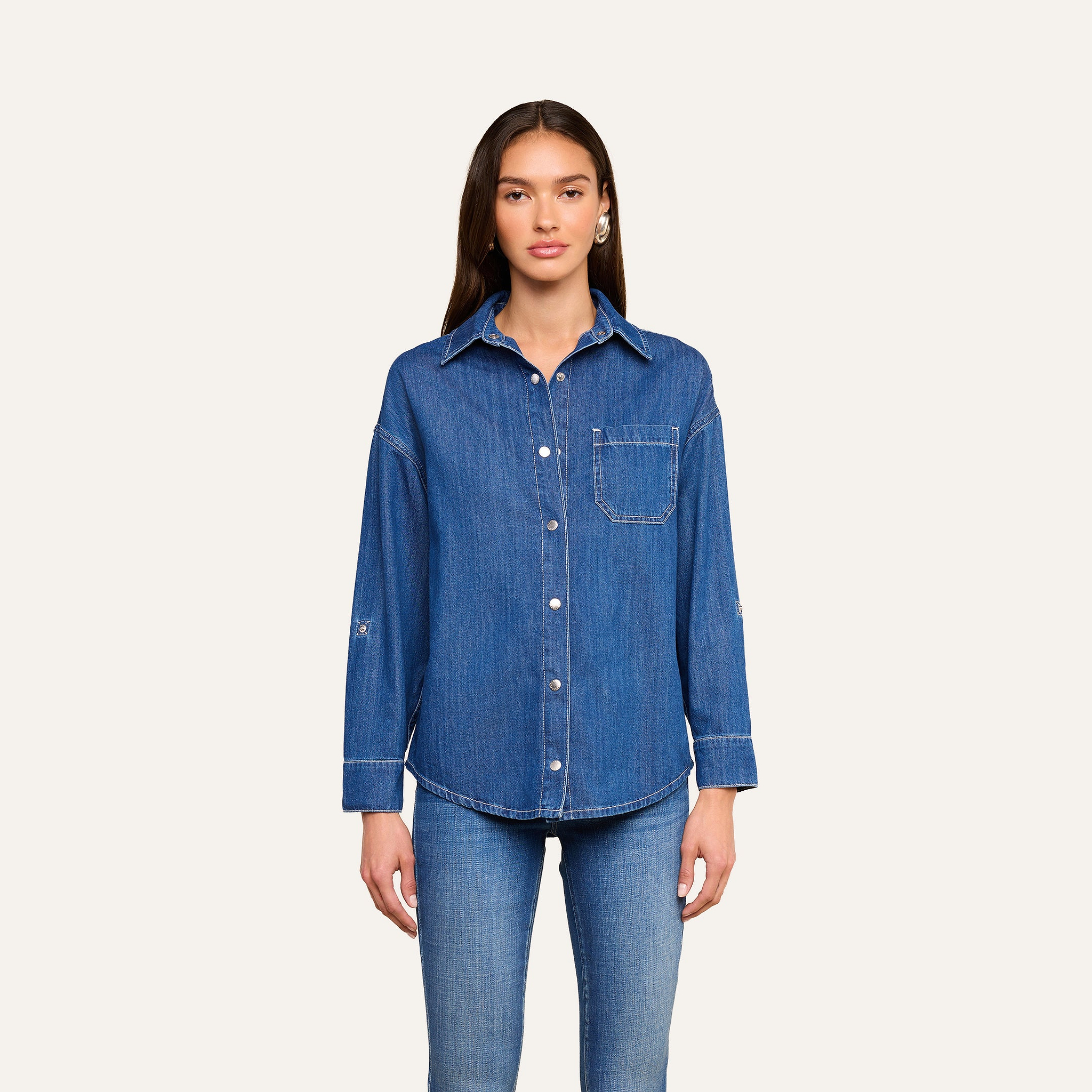 A woman stands against a plain background, wearing the Jorah Oversized Shirt—a featherweight denim button-up with a front pocket—paired with matching blue jeans. She has long, straight hair and faces forward with a neutral expression.