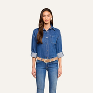 A woman with long brown hair wears the Jorah Oversized Shirt with rolled sleeves, paired with blue jeans, a beige belt, and earrings. She stands facing forward against a plain light background.