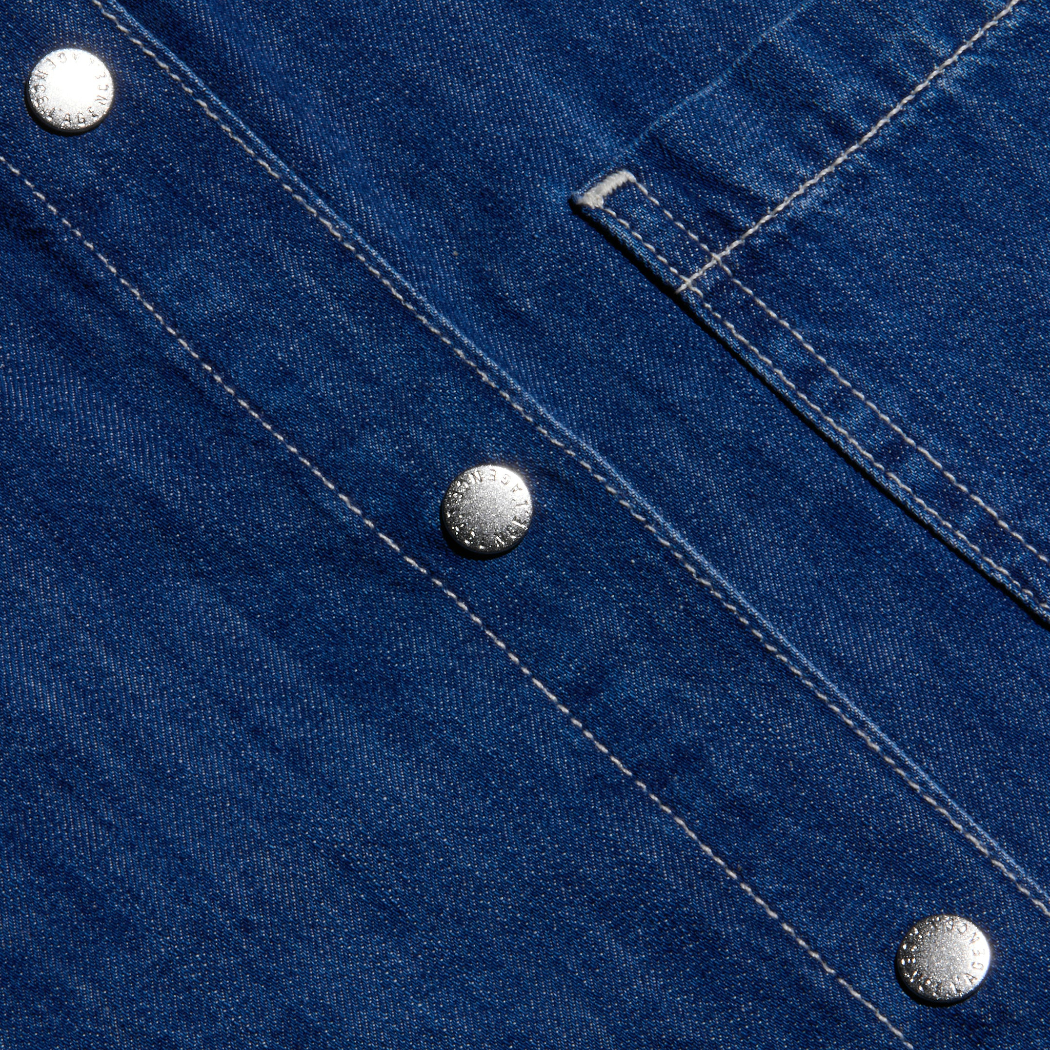 Close-up of the indigo featherweight denim fabric on the Jorah Oversized Shirt, featuring visible white stitching, three silver snap buttons, and part of its oversized pocket flap.