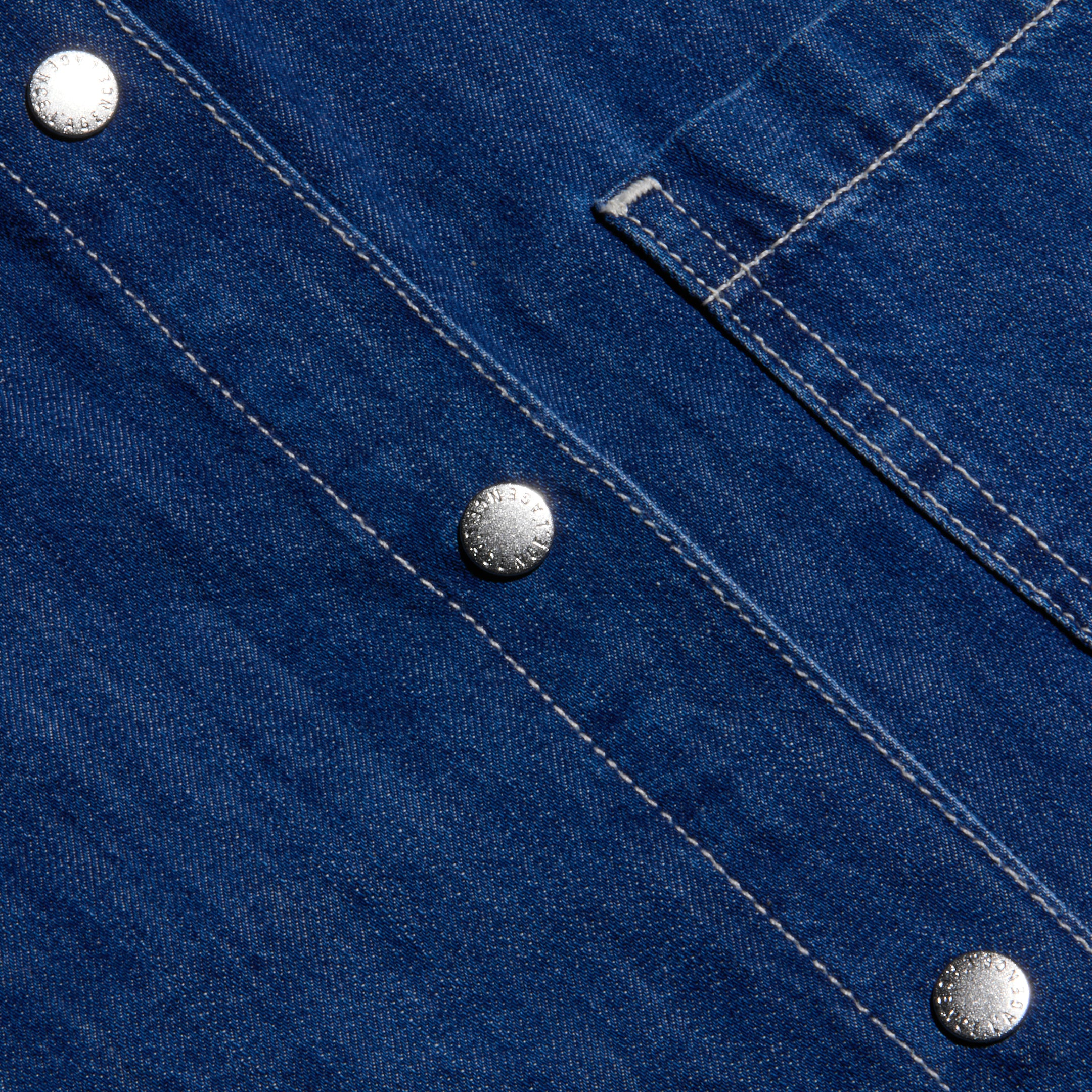 Close-up of the indigo featherweight denim fabric on the Jorah Oversized Shirt, featuring visible white stitching, three silver snap buttons, and part of its oversized pocket flap.