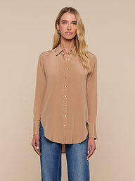 A person wearing the Babette Silk Blouse in light brown, featuring a relaxed fit and button-up design, paired with blue jeans, stands facing forward against a plain, light background.