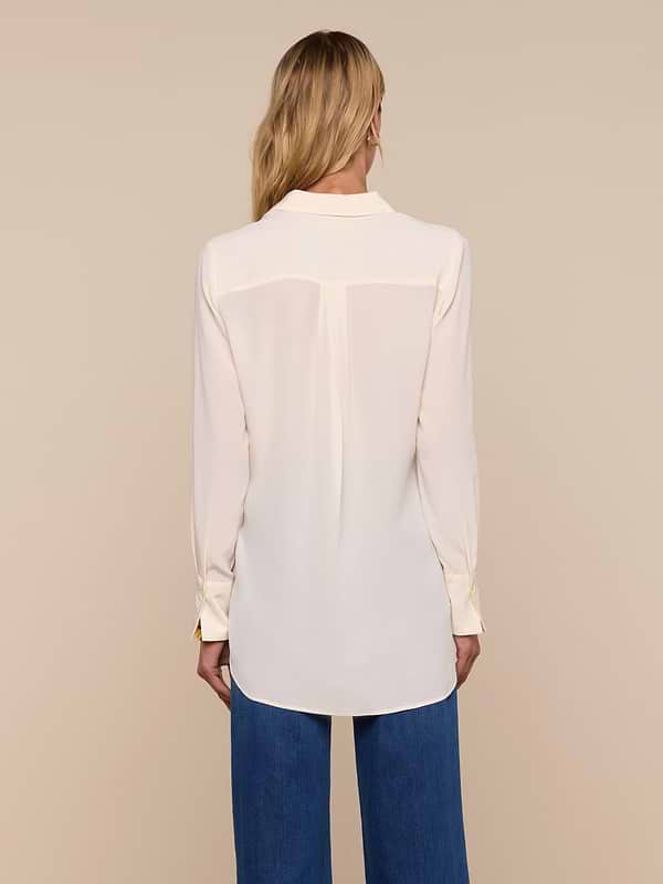 A woman with long blonde hair is wearing the Babette Silk Blouse—a cream-colored, relaxed fit silk top—paired with blue jeans, standing with her back to the camera against a plain white background.