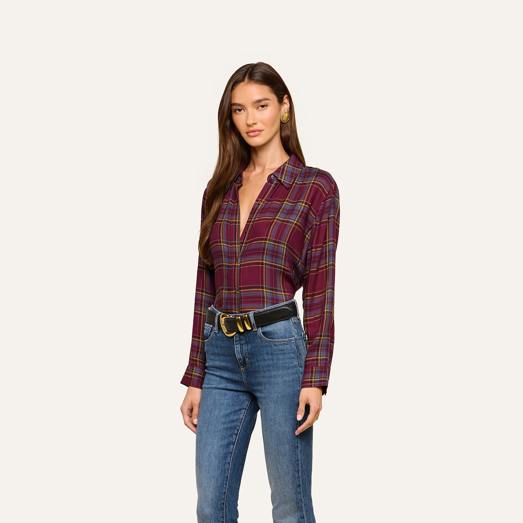A woman models the Suzette Shirt, a maroon plaid button-down, tucked into blue jeans with a black belt. She stands against a plain light background and looks at the camera in a relaxed pose.