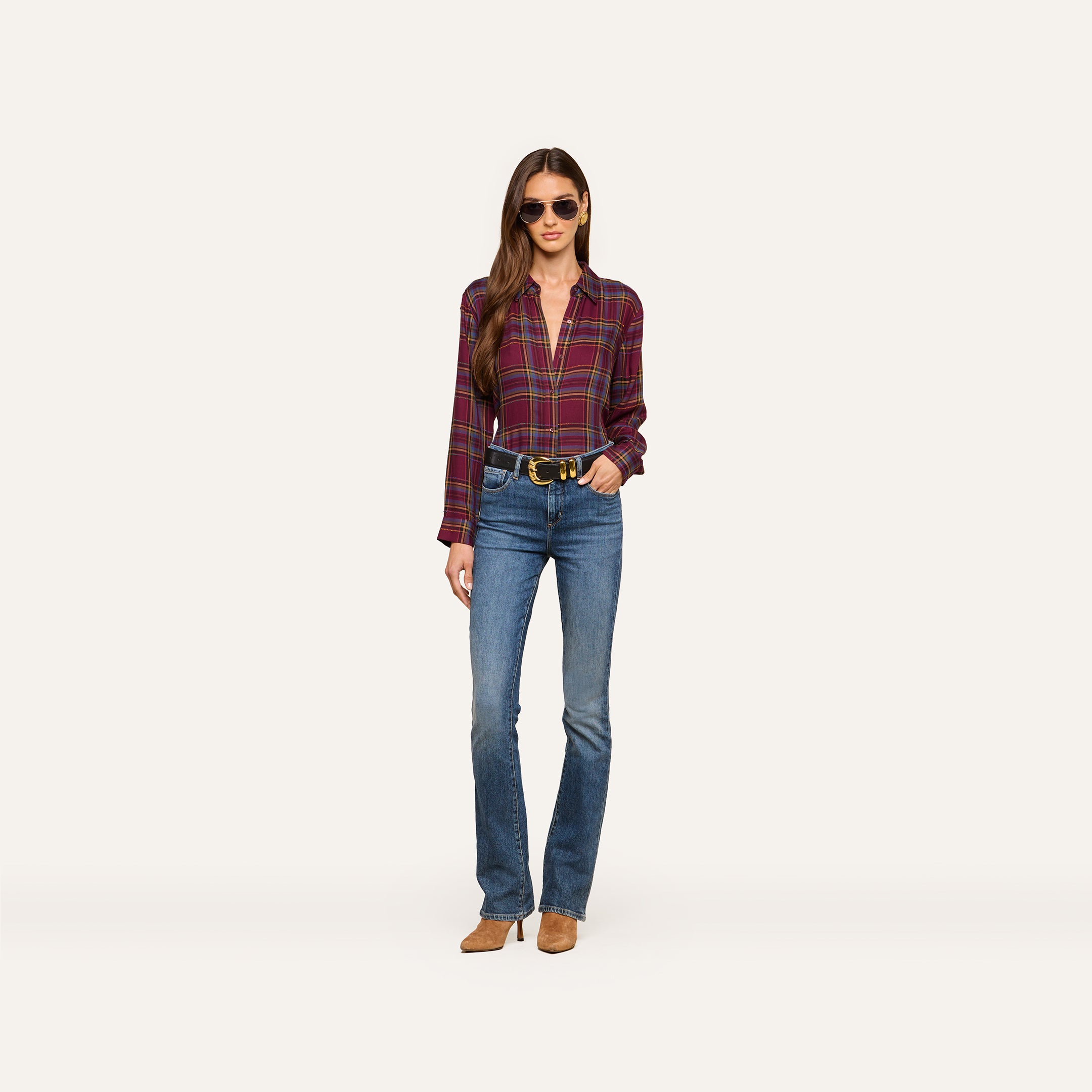 A woman wears the Suzette Shirt with sunglasses, blue jeans, a black belt, and brown shoes as she stands against a plain white background.