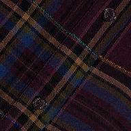 Close-up of the Suzette Shirt in dark red, blue, yellow, and beige plaid tones with two black buttons visible, featuring diagonal stitching and detailed texture.