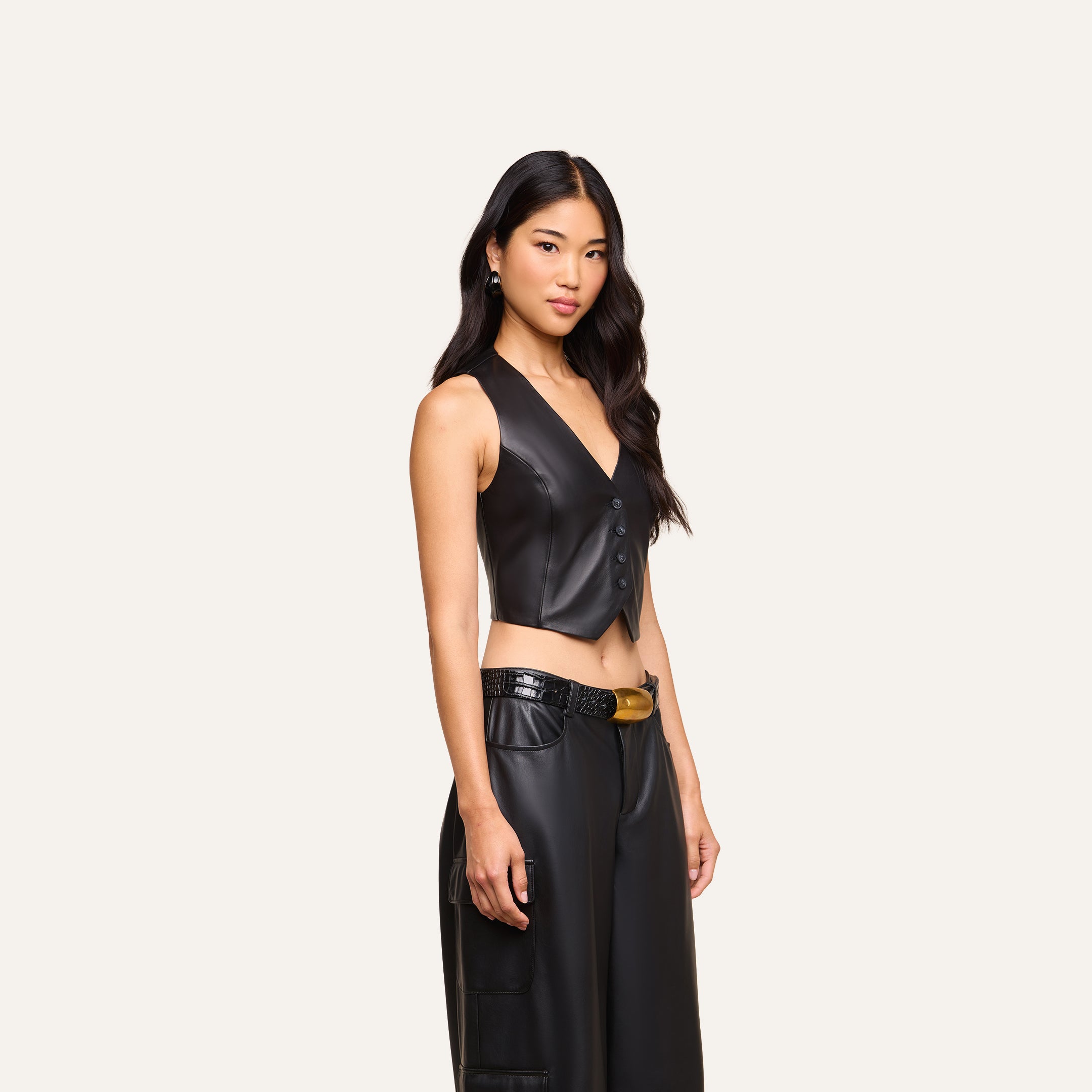 A woman with long black hair wears the Jianna Leather Vest paired with matching black leather pants, standing against a plain light background. Her look channels the edgy style seen at New York Fashion Week for Fall 2026.