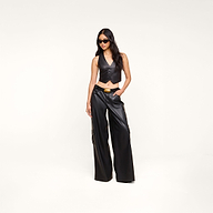 A woman wearing sunglasses, the Jianna Leather Vest, and matching black leather wide-leg pants stands with one hand in her pocket against a plain white background—a look inspired by Fall 2026 fashion at New York Fashion Week.