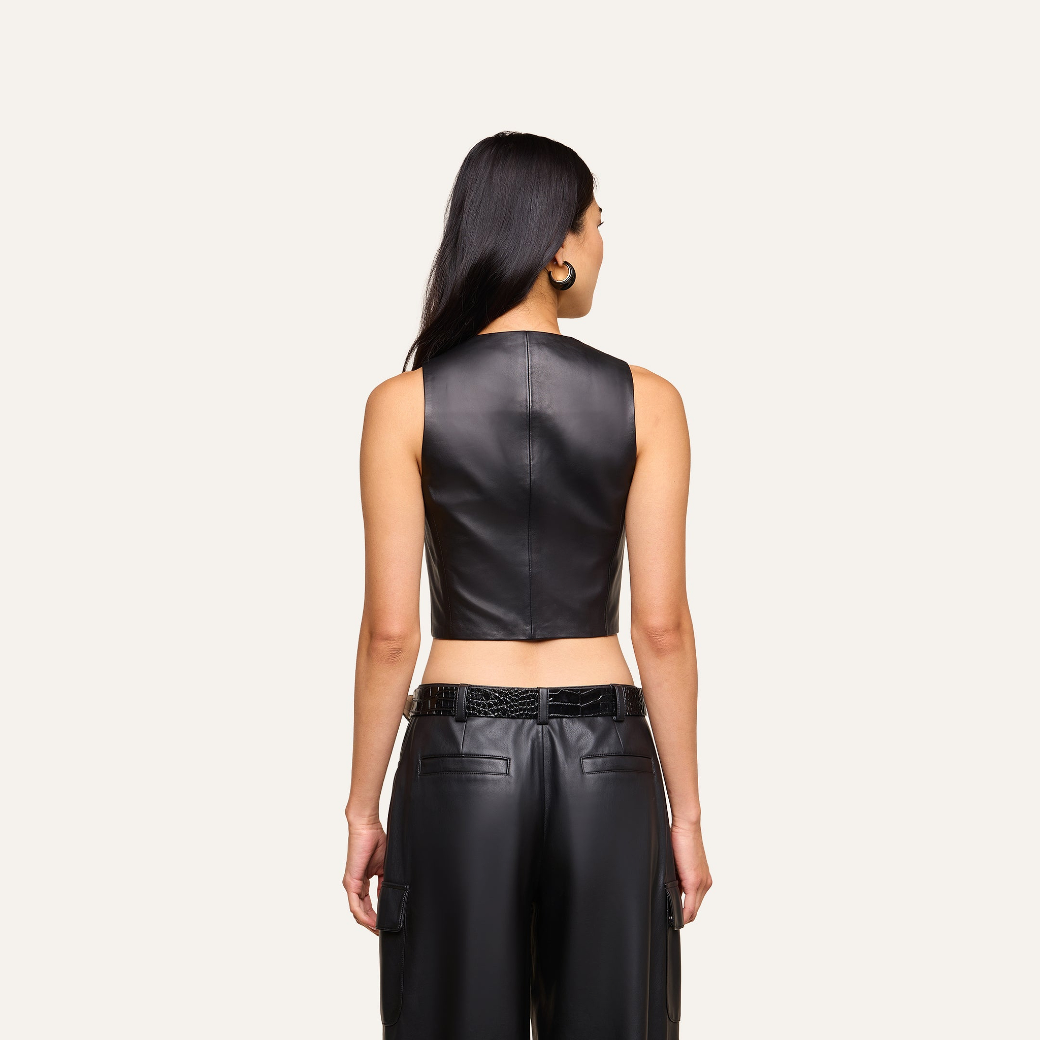 A woman with long dark hair, seen from behind, wears the sleeveless black Jianna Leather Vest paired with black leather pants against a plain light background—an edgy look inspired by Fall 2026 fashion.