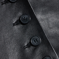 Close-up of the Jianna Leather Vest, featuring black leather fabric with several black buttons sewn in a vertical row, highlighting both the rich texture and detailed stitching around each button on this cropped design inspired by Fall 2026 fashion.