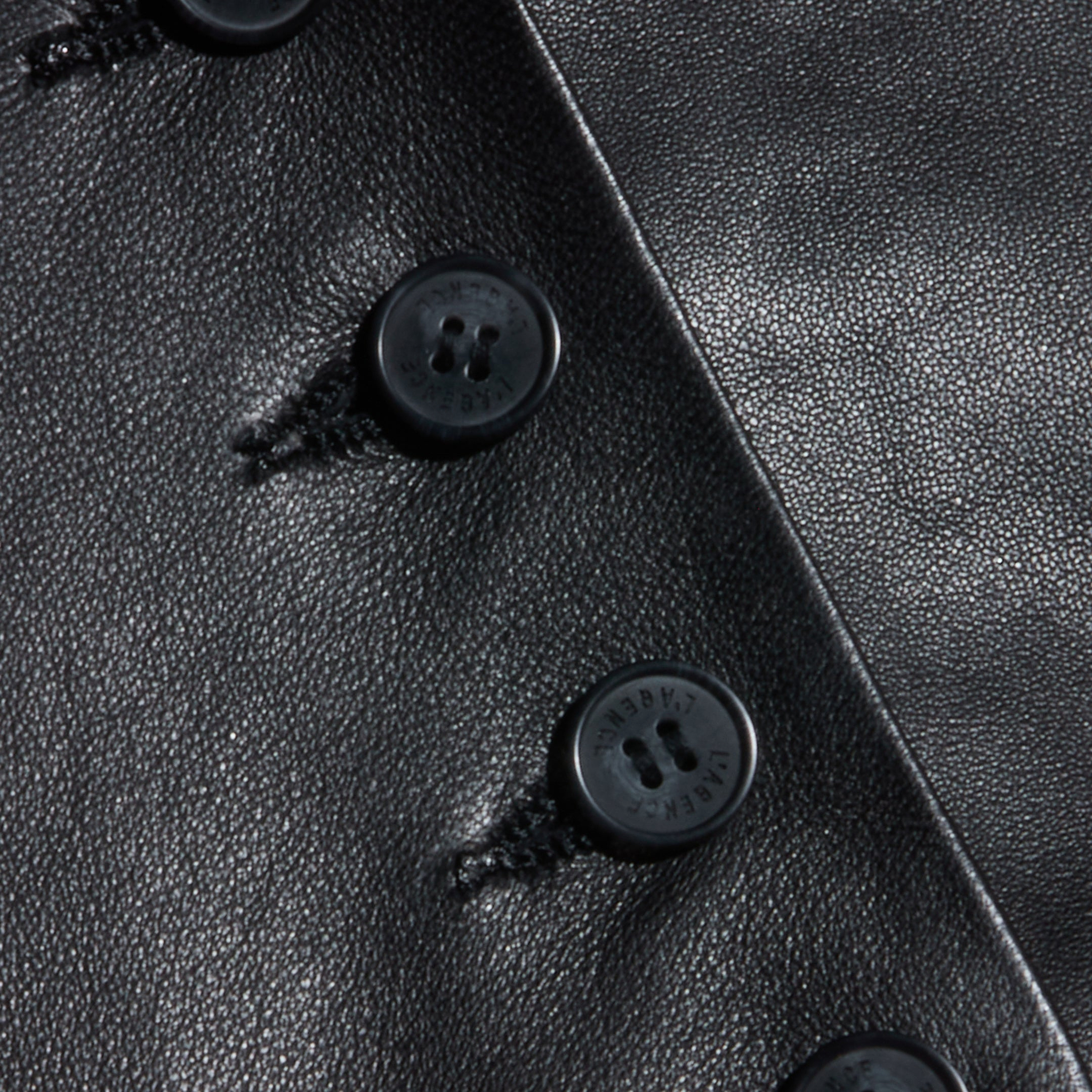 Close-up of the Jianna Leather Vest, featuring black leather fabric with several black buttons sewn in a vertical row, highlighting both the rich texture and detailed stitching around each button on this cropped design inspired by Fall 2026 fashion.