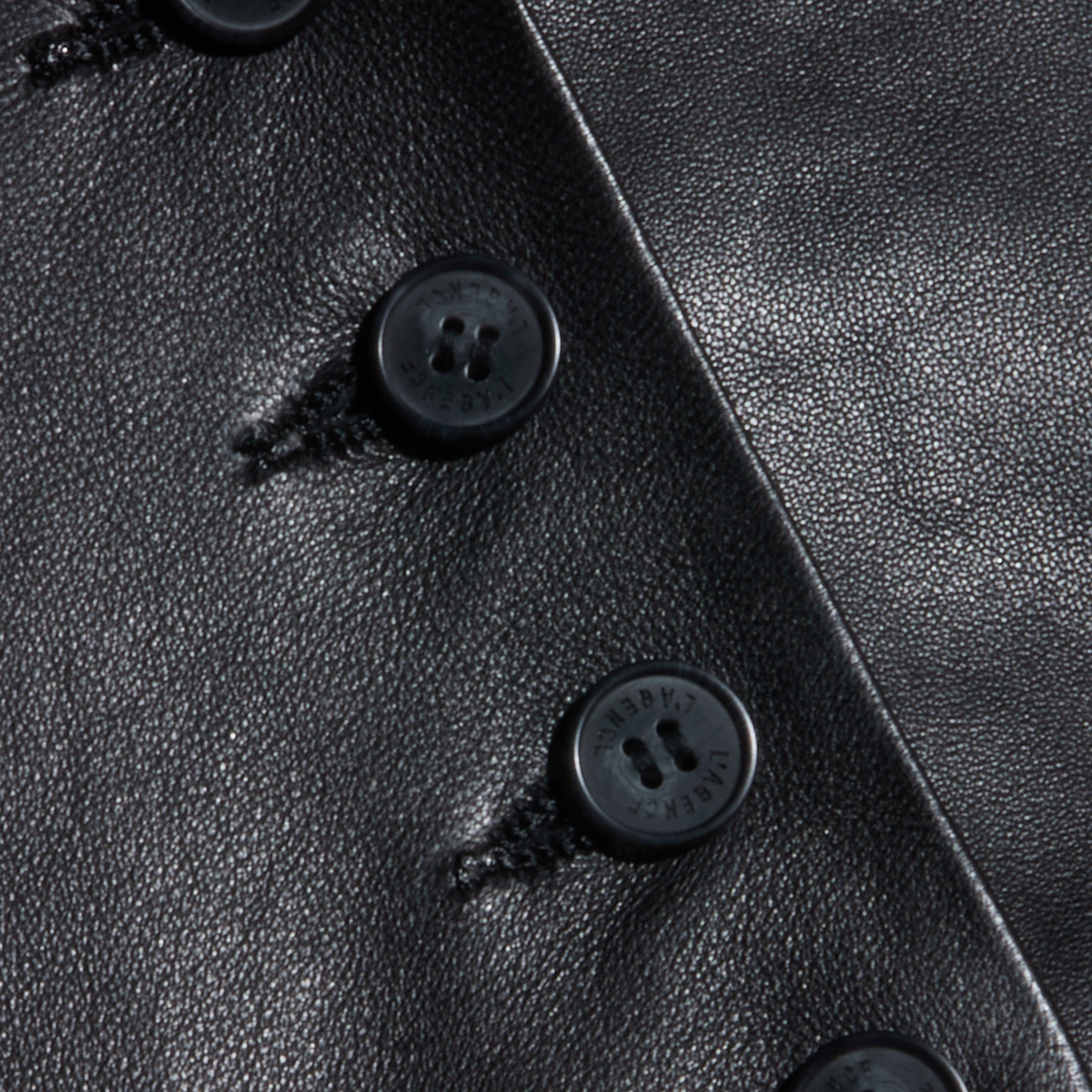 Close-up of the Jianna Leather Vest, featuring black leather fabric with several black buttons sewn in a vertical row, highlighting both the rich texture and detailed stitching around each button on this cropped design inspired by Fall 2026 fashion.