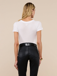 A woman with long blonde hair is seen from behind, wearing the Becca Cotton V-Neck Tee in white, tucked into high-waisted black pants with a black belt, against an off-white background.