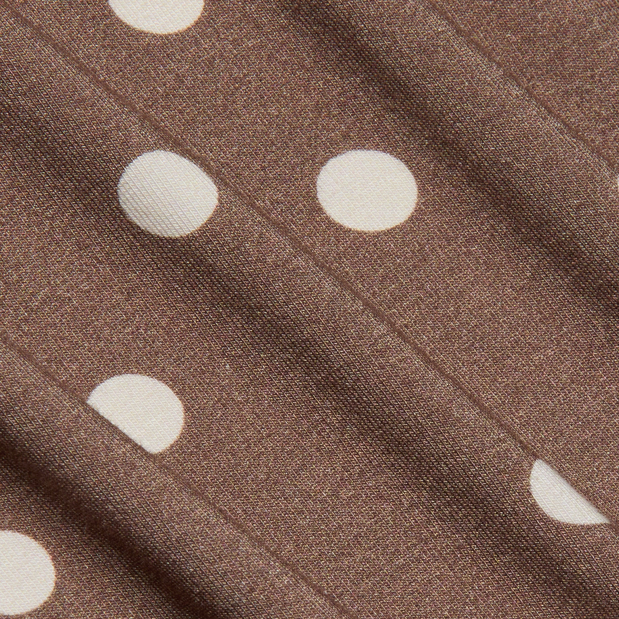 Close-up of the Ressi Fitted Tee in brown stretch jersey knit fabric featuring white, evenly spaced polka dots and subtle diagonal folds that highlight the fabric’s texture.