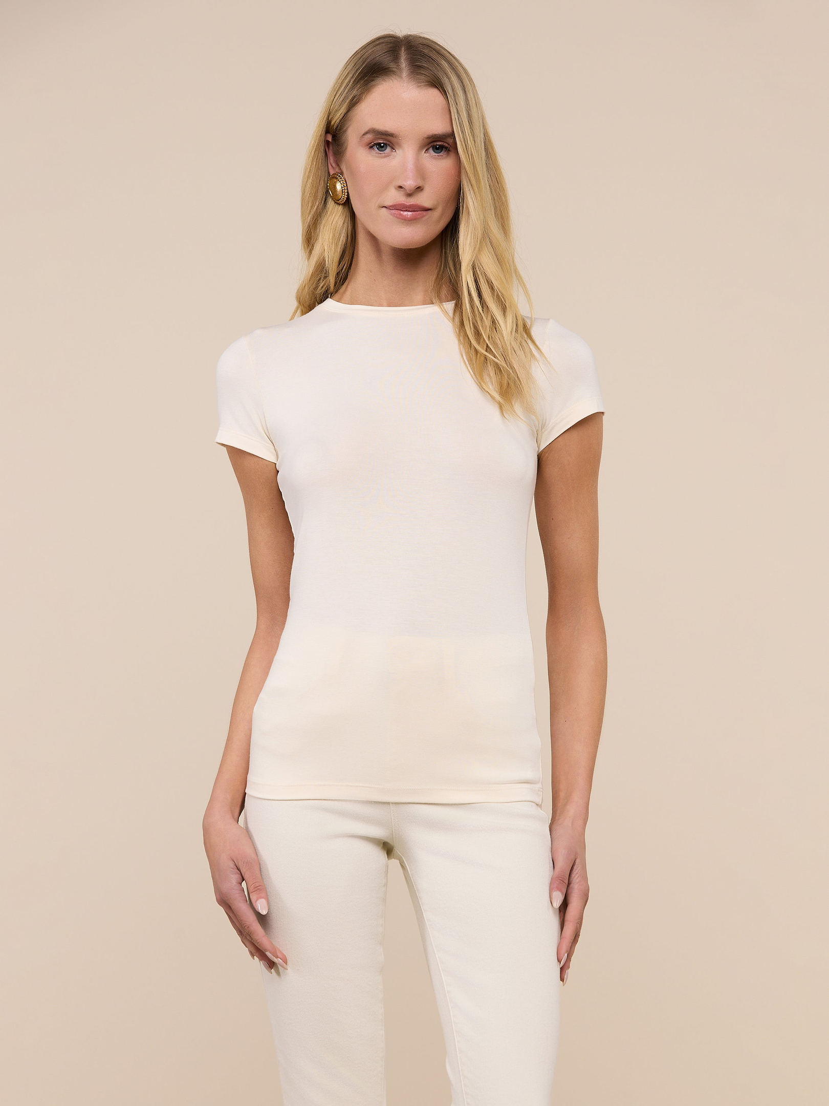 A woman with long blonde hair stands against a plain, light background, facing forward with a neutral expression, wearing the Ressi Fitted Tee in vintage white and matching pants.