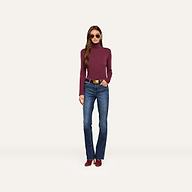 A woman wearing sunglasses, the Lani Turtleneck in a slim fit burgundy shade, blue jeans with a belt, and matching burgundy shoes stands facing forward against a plain light background.