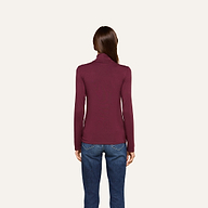 A woman stands facing away, wearing the slim fit Lani Turtleneck in maroon paired with blue jeans against a plain, light background—a perfect look for Fall 2026.