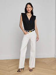 A woman stands against a plain background in a sleeveless black Akari Bodysuit, paired with white wide-leg pants, a black belt, black heels, and a gold necklace. With one hand in her pocket, she poses in a relaxed manner.