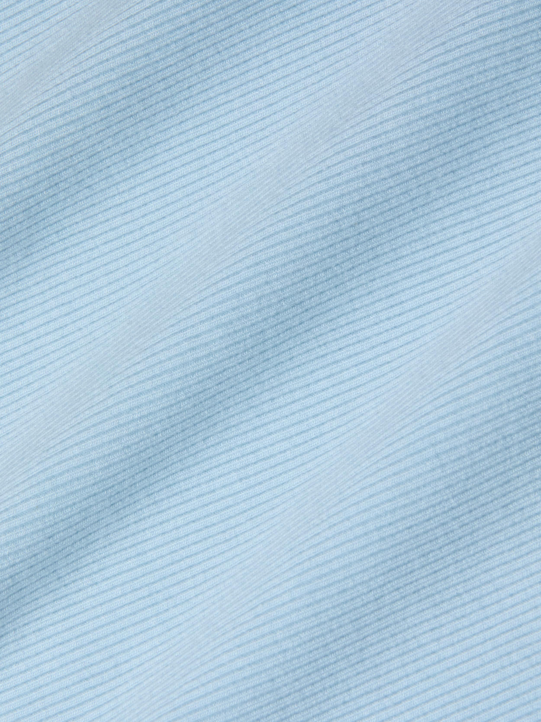 Close-up of the Nica Scoopneck Bodysuit in light blue, featuring fine, diagonal, evenly spaced lines that create a subtle striped pattern. The high recovery stretch rib enhances the soft and smooth texture, giving the fabric a gentle and calming visual effect.