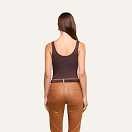 A woman stands facing away, wearing a dark brown Nica Scoopneck Bodysuit and tan pants with pockets. Her straight brown hair is down, and she is positioned against a plain light background.