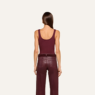 A woman with straight brown hair, seen from behind against a plain light background, wears a sleeveless maroon Nica Scoopneck Bodysuit paired with matching maroon leather pants.