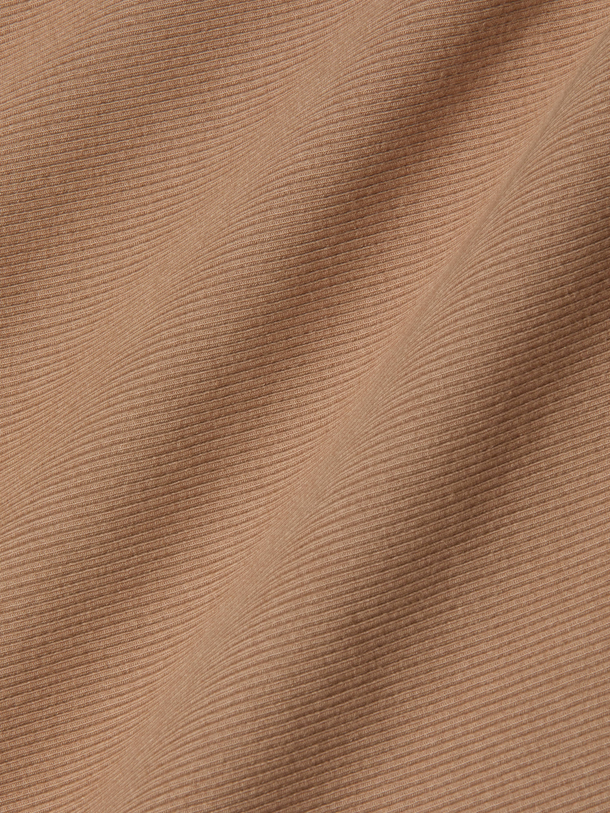 Close-up of the Adira Tank’s light brown ribbed fabric, with diagonal folds and fine textured lines that highlight the intricate pattern and soft surface of this essential piece.