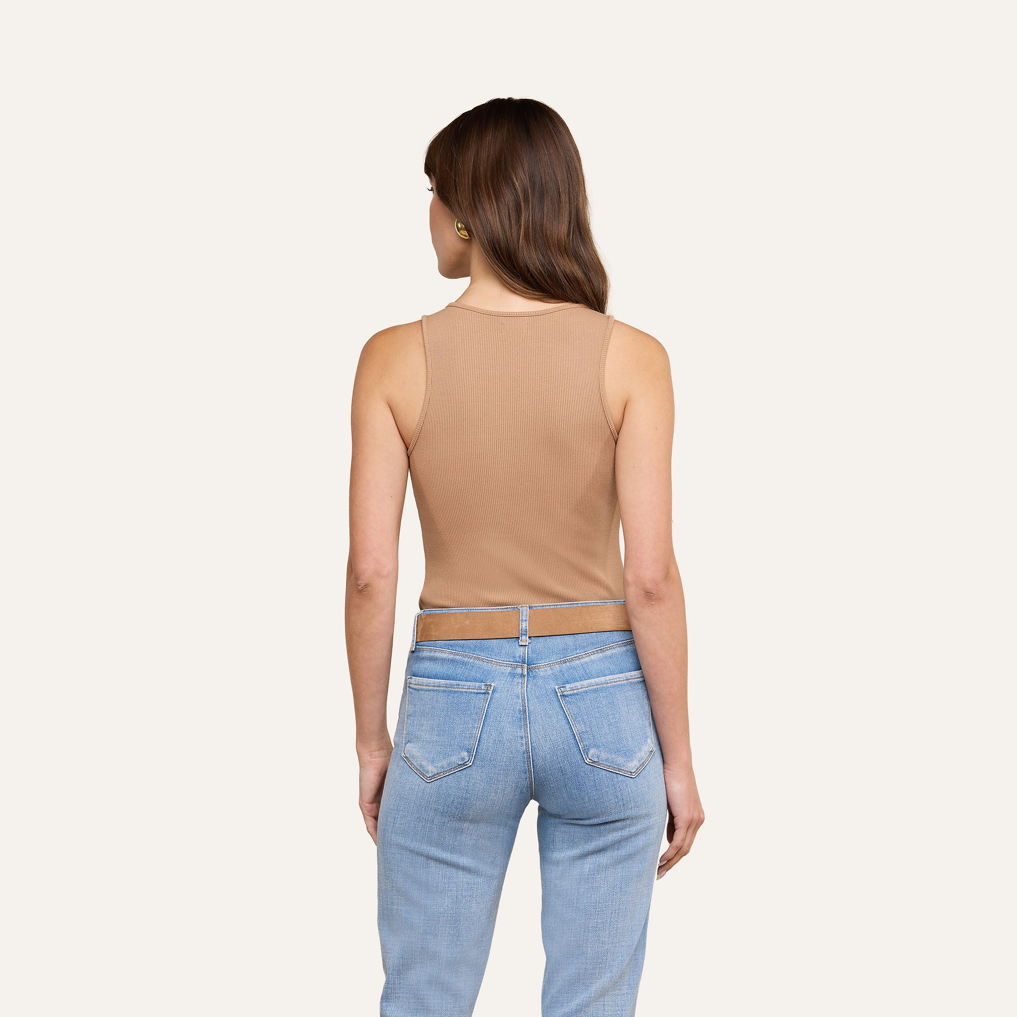 Une femme, de dos à la caméra, porte le débardeur Adira en maille côtelée extensible et un jean bleu clair, sur un fond beige uni.