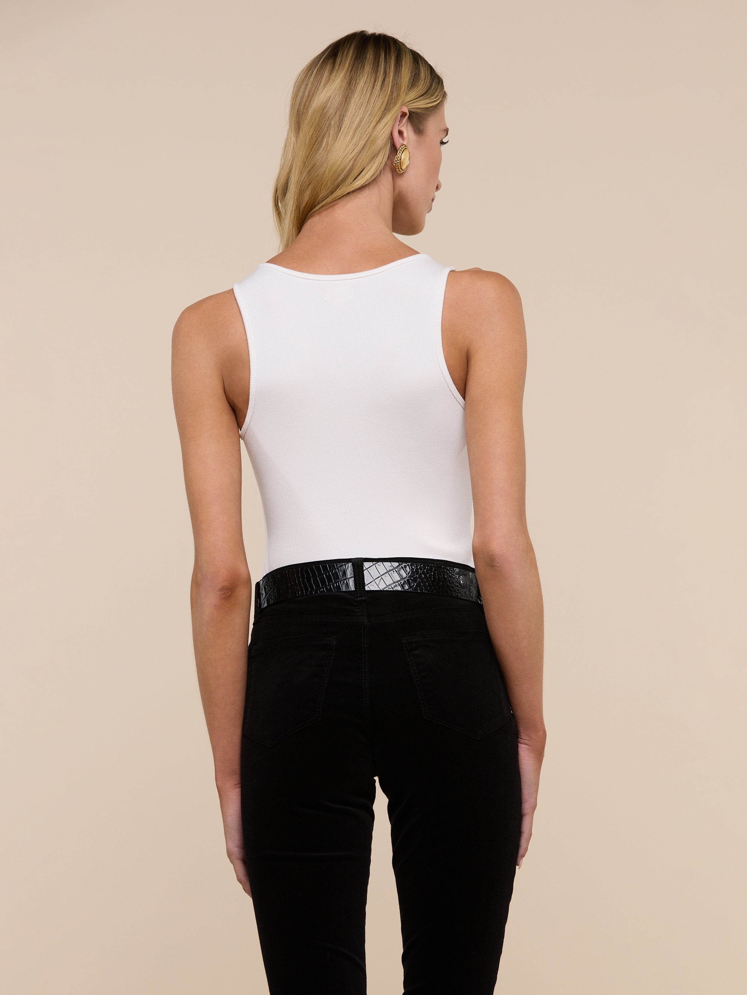 A person with long blonde hair is standing with their back to the camera, wearing the Adira Scoopneck Tank and blue jeans against a plain light background.