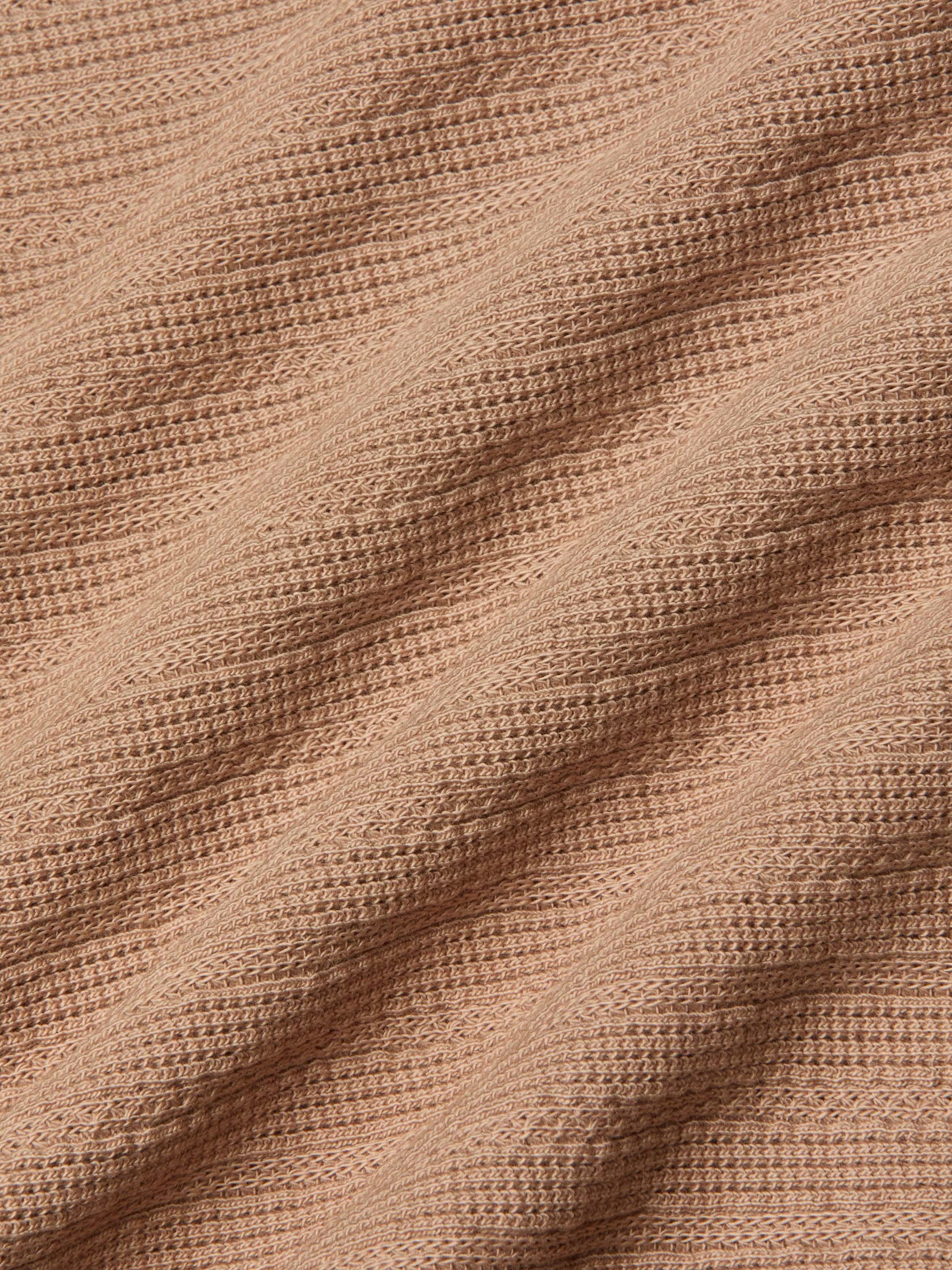 Close-up of the Adira Scoopneck Tank in peach-colored organic cotton, featuring a ribbed, textured pattern in diagonal lines. The soft material is slightly stretched, highlighting the details of the individual knit stitches.
