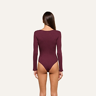 A woman with long brown hair is standing facing away, wearing a maroon Elara Scoopneck Bodysuit made from stretch cotton modal and designed for a body-contouring fit, set against a plain light background.