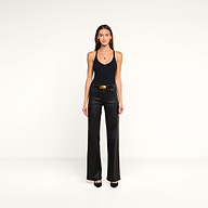 A woman stands against a plain white background, wearing the Wrenna Racerback Bodysuit in black rib fabric, paired with black leather pants, a black belt with a large buckle, and black heels. Her long straight hair frames her neutral expression.